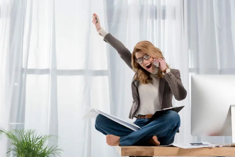 happy businesswoman with papers talking on smartphone while sitting on table in office - workplace flexibility